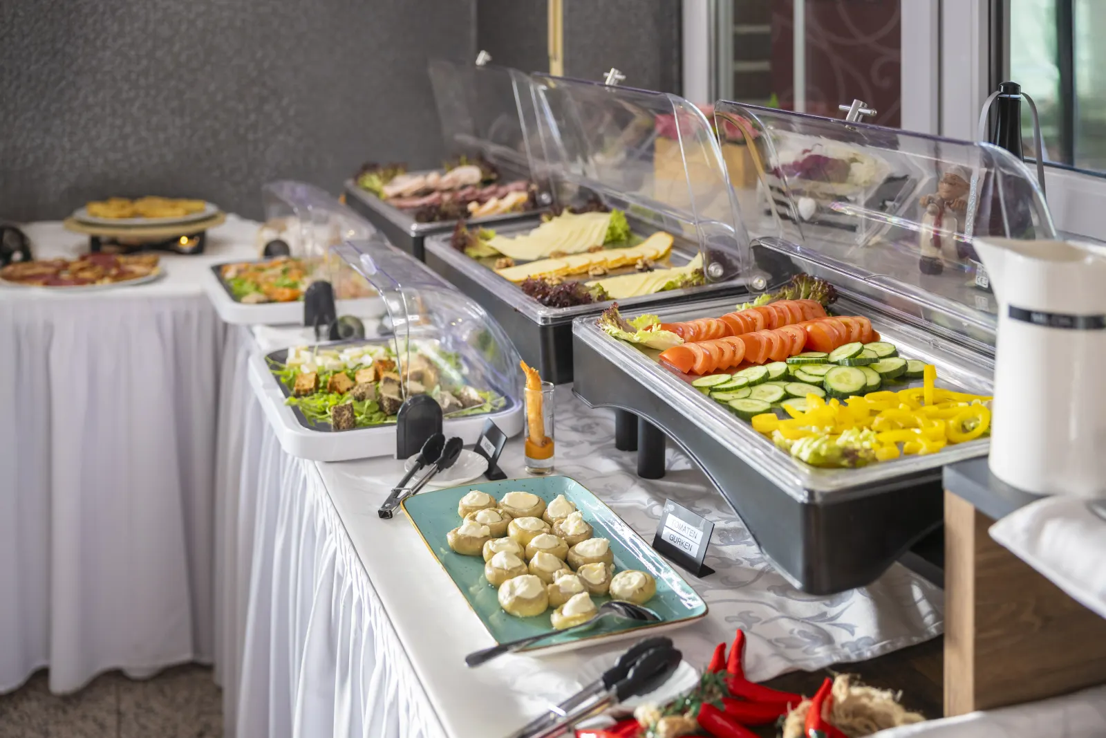 Buffet mit Salaten, Gemüse, Käse, Aufschnitt und warmen Speisen unter Glashauben