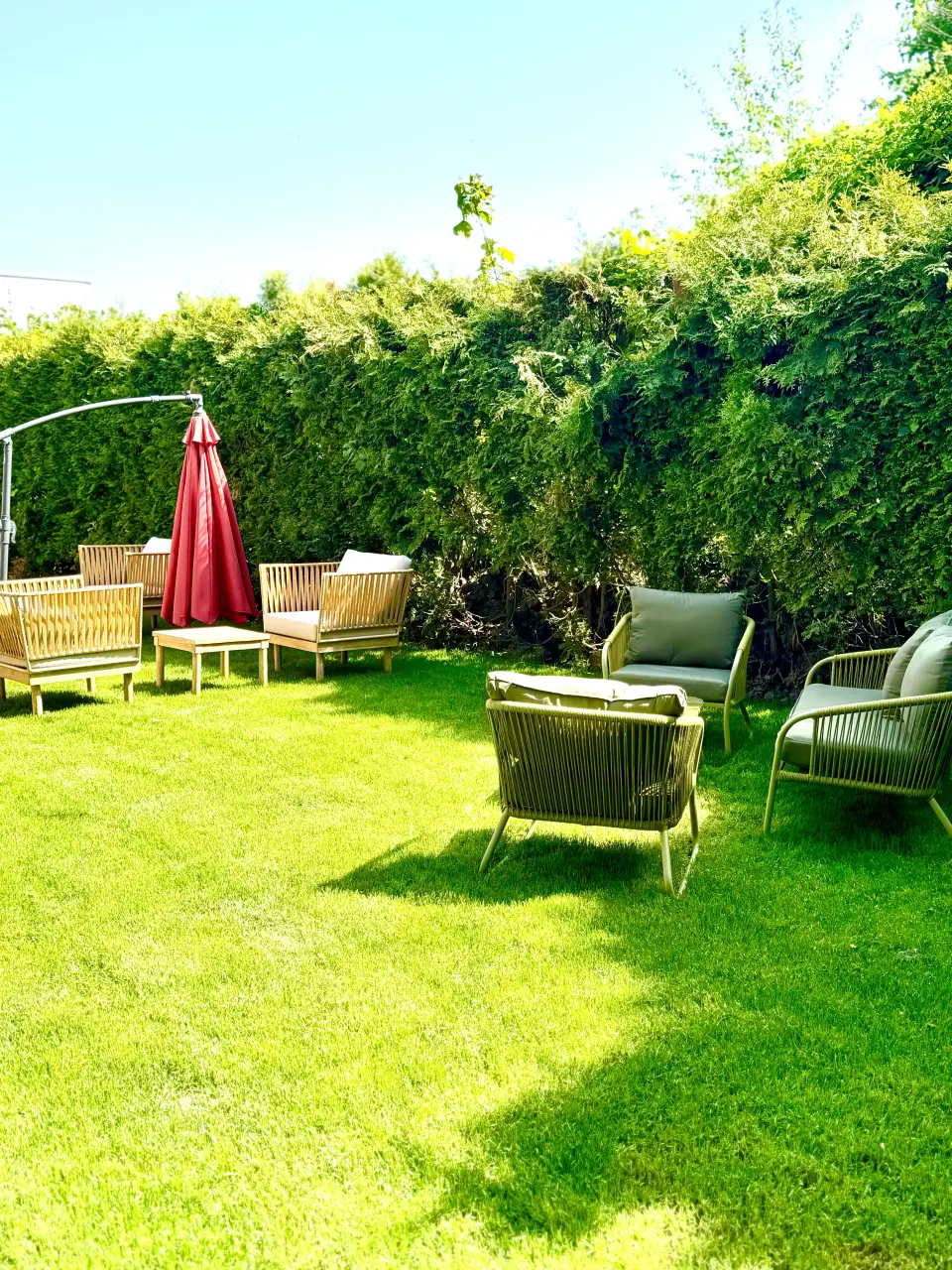 Lounge-Sessel und Sonnenschirm im Garten vor einer grünen Hecke